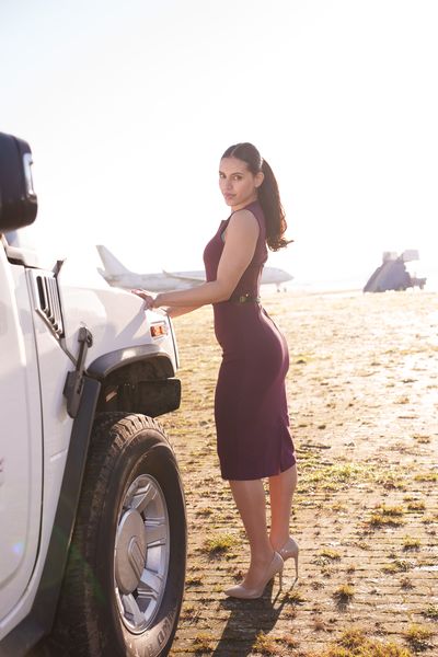 Private jet fashion shoot organised by Marsha Bagmeijer, model in a burgundy dress beside a white Hummer with private jets behind her